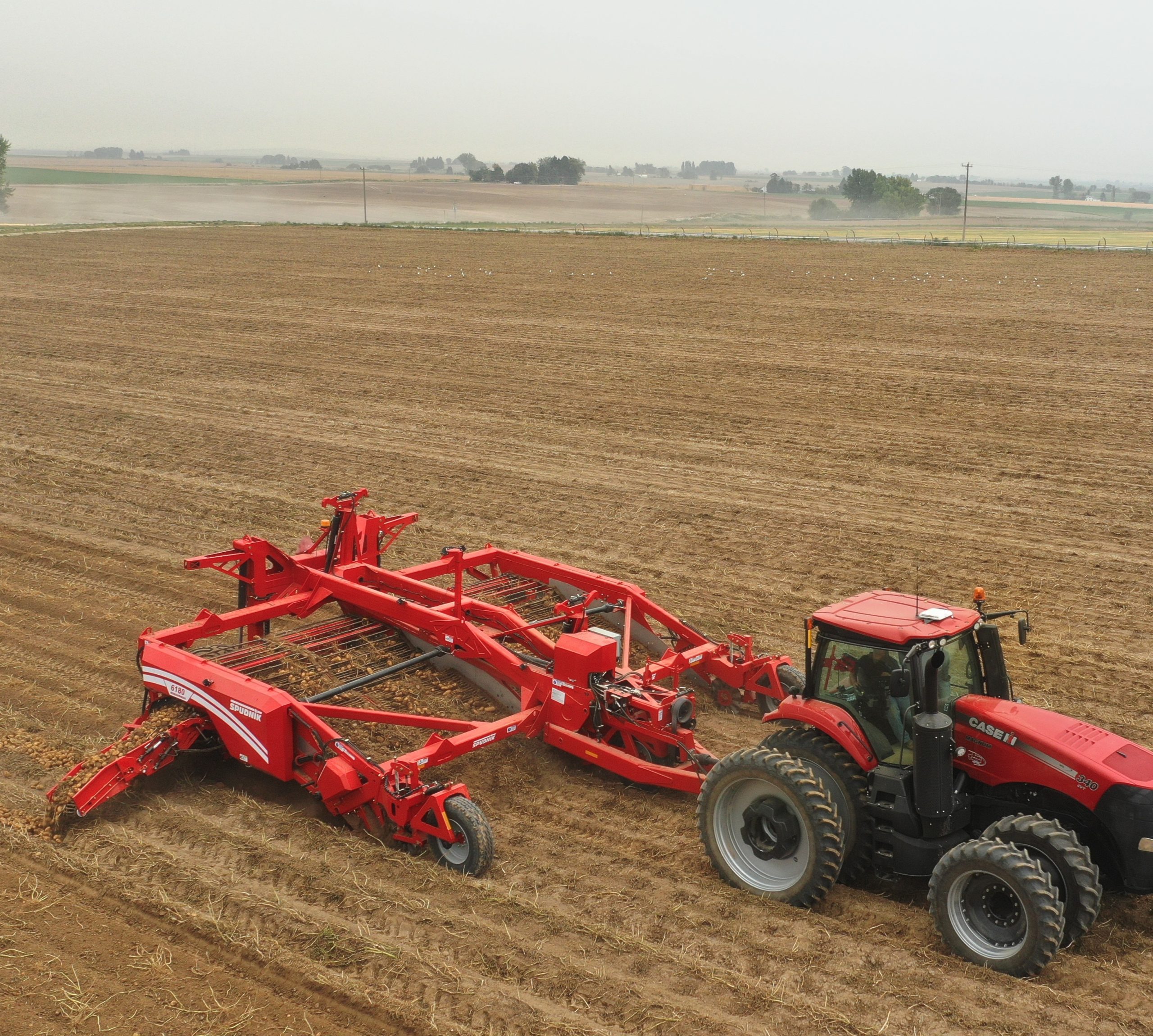 Man in a tractor attached to a potato harvester, harvesting potatoes on a big farm.