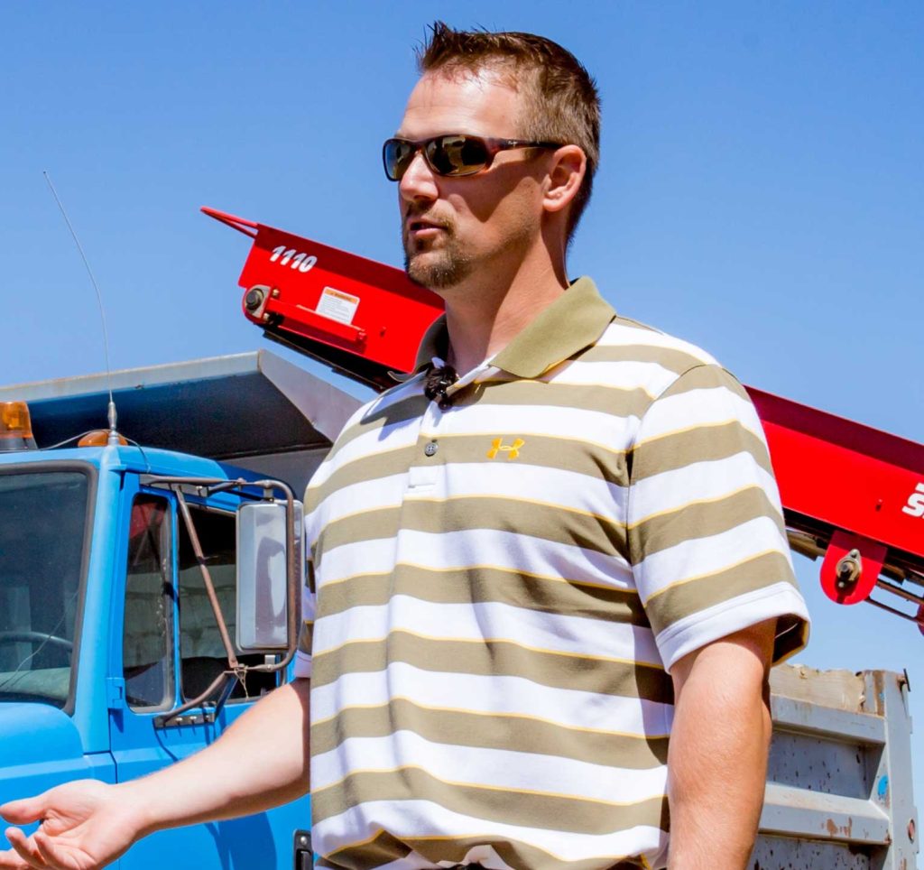 Man standing by a dumping truck and Spudnik piece of farming equipment.