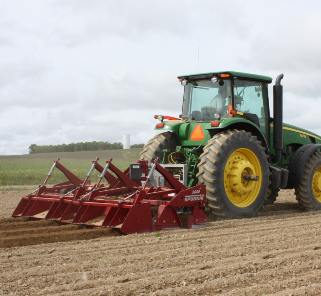 Spudnik's 4 Row Ridge Potato Hiller attached to a tractor in a farm.