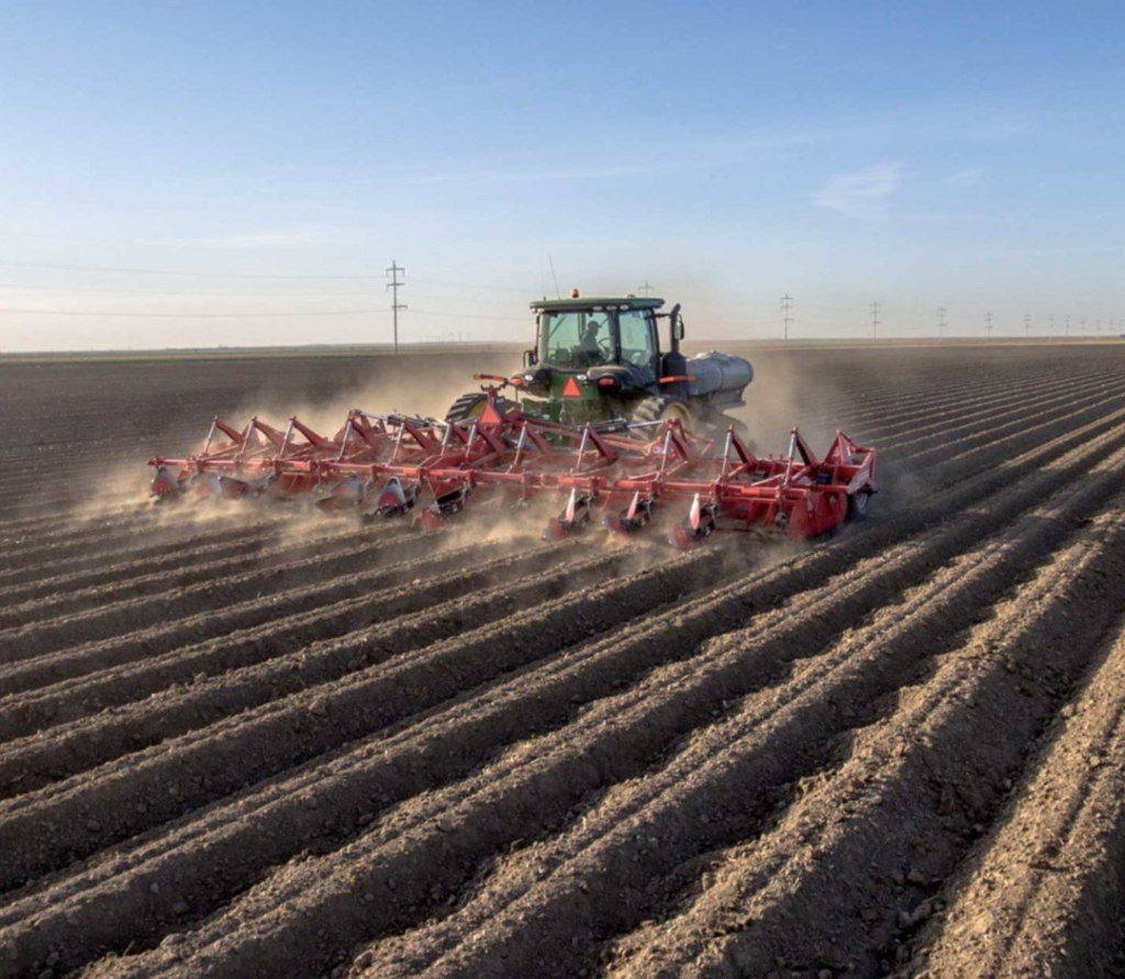 Spudnik's 8 Row Ridge Potato Hiller and a John Deere tractor at work in a farm.