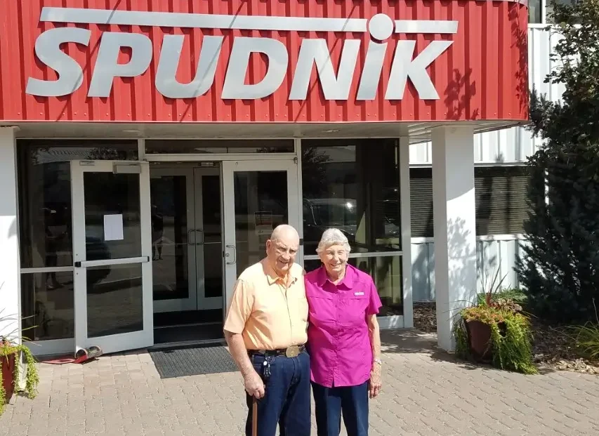 Carl Hobbs, Co-founder of Spudnik Equipment Company with his wife posing for a picture in front of a Spudnik Equipment's main office.